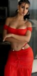 Woman posing in a red off-the-shoulder two-piece outfit indoors with arms crossed.